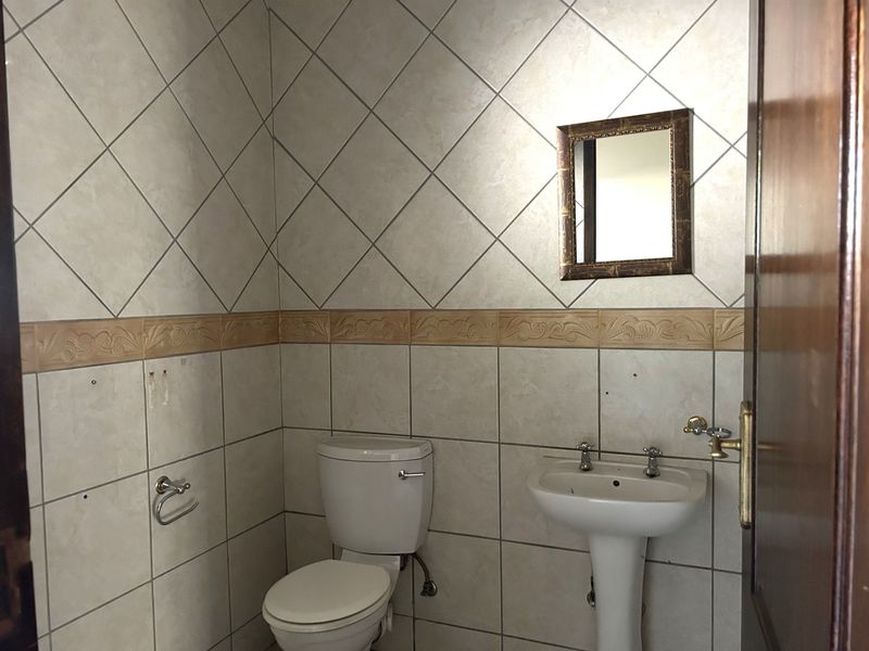 A functional bathroom featuring a pedestal sink, toilet, and decorative ceramic wall tiling with a neutral color palette.