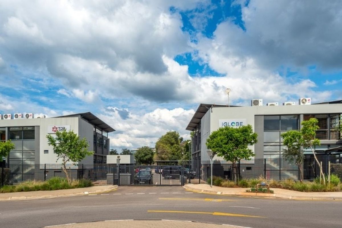 Front view of a modern office complex featuring dual buildings, secure gated access, paved driveway, and well-maintained landscaping.