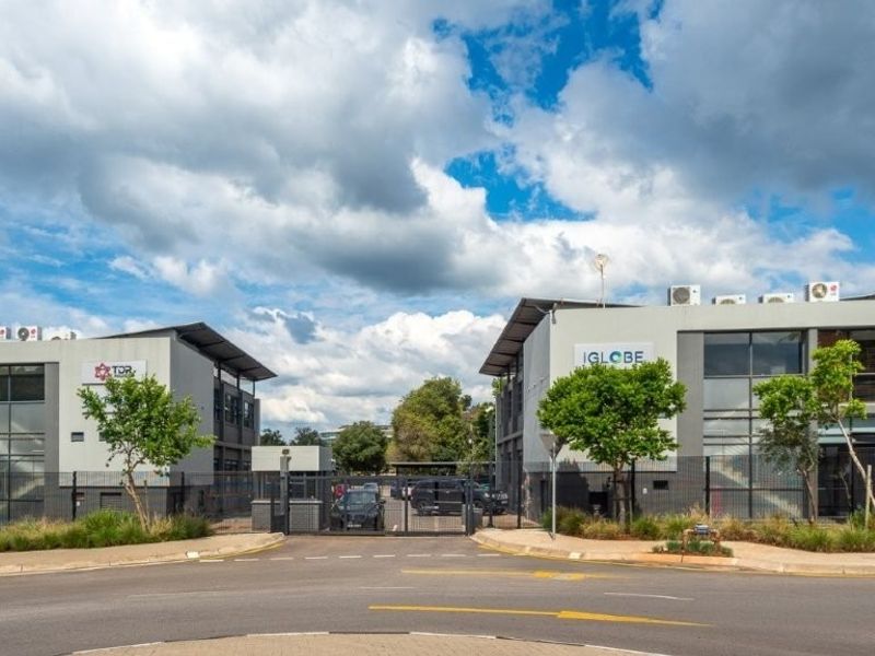 Front view of a modern office complex featuring dual buildings, secure gated access, paved driveway, and well-maintained landscaping.