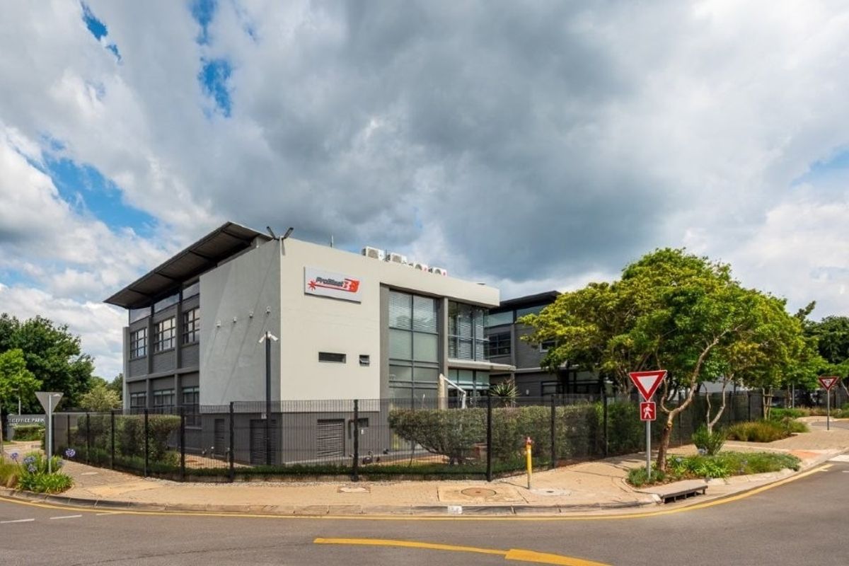 A modern multi-story office building featuring a contemporary facade, secure perimeter fencing, and integrated air conditioning units, situated on a corner lot.