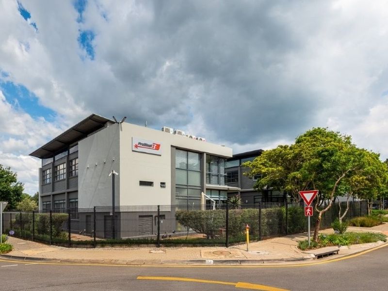A modern multi-story office building featuring a contemporary facade, secure perimeter fencing, and integrated air conditioning units, situated on a corner lot.