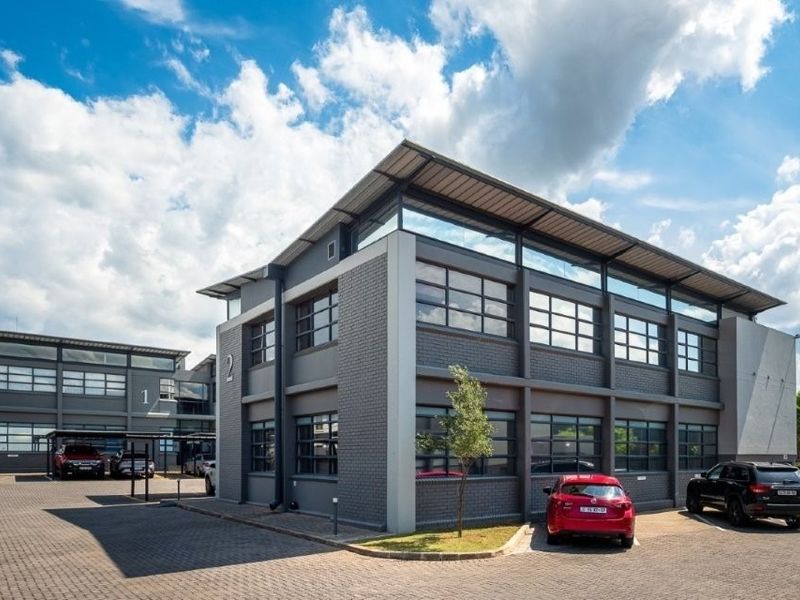 Modern multi-story office building featuring a contemporary grey brick facade, large windows, and paved parking area.