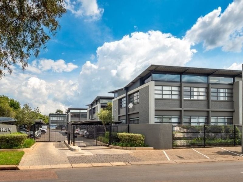 A professional exterior view of the Queens Office Park, featuring modern architecture, secure gated access, paved parking areas, and well-maintained landscaping.