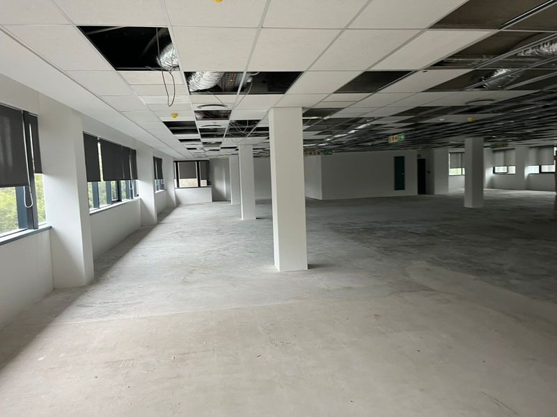 An expansive, open-plan office space currently in a shell condition with exposed ceiling grid, structural columns, and unfinished flooring.