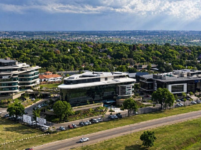 Aerial view of a modern office park complex featuring multiple glass-facade buildings, landscaped surroundings, and extensive parking facilities.