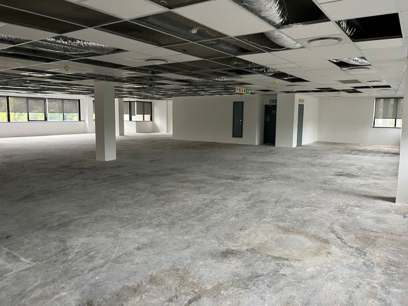 A large, open-plan office space featuring an unfinished concrete floor and a partially installed suspended ceiling with exposed HVAC ducting.