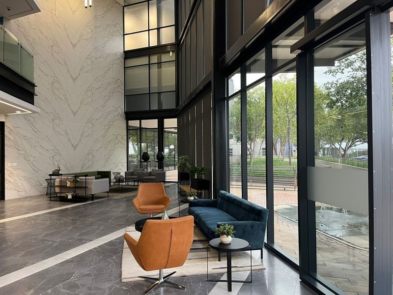 Modern double-volume office lobby featuring floor-to-ceiling glass windows, marble-look tile flooring, and a striking marble-clad feature wall.