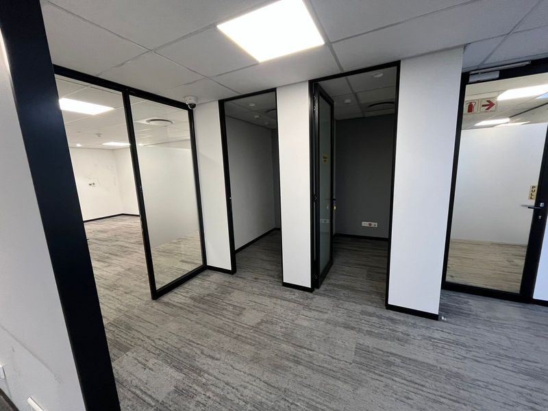 Modern office space featuring glass partitions, carpeted flooring, and recessed lighting, providing a clean and professional environment for business operations.