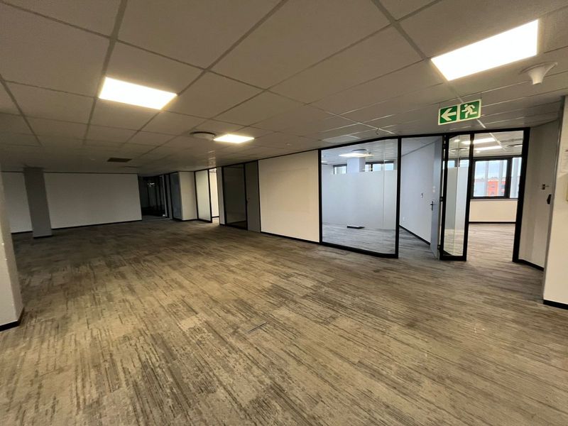Spacious open-plan office area featuring suspended ceilings, recessed lighting, carpeted flooring, and modern glass partition walls for private office spaces.