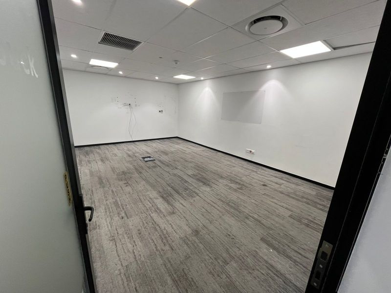 A vacant, well-lit office space featuring a suspended ceiling, recessed lighting, air conditioning, and grey carpet tiles, ready for immediate commercial use.