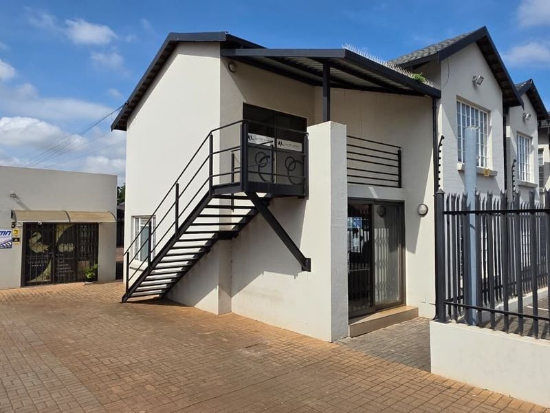 Front exterior view of a commercial office building featuring a paved driveway, external metal staircase, and secure perimeter fencing.