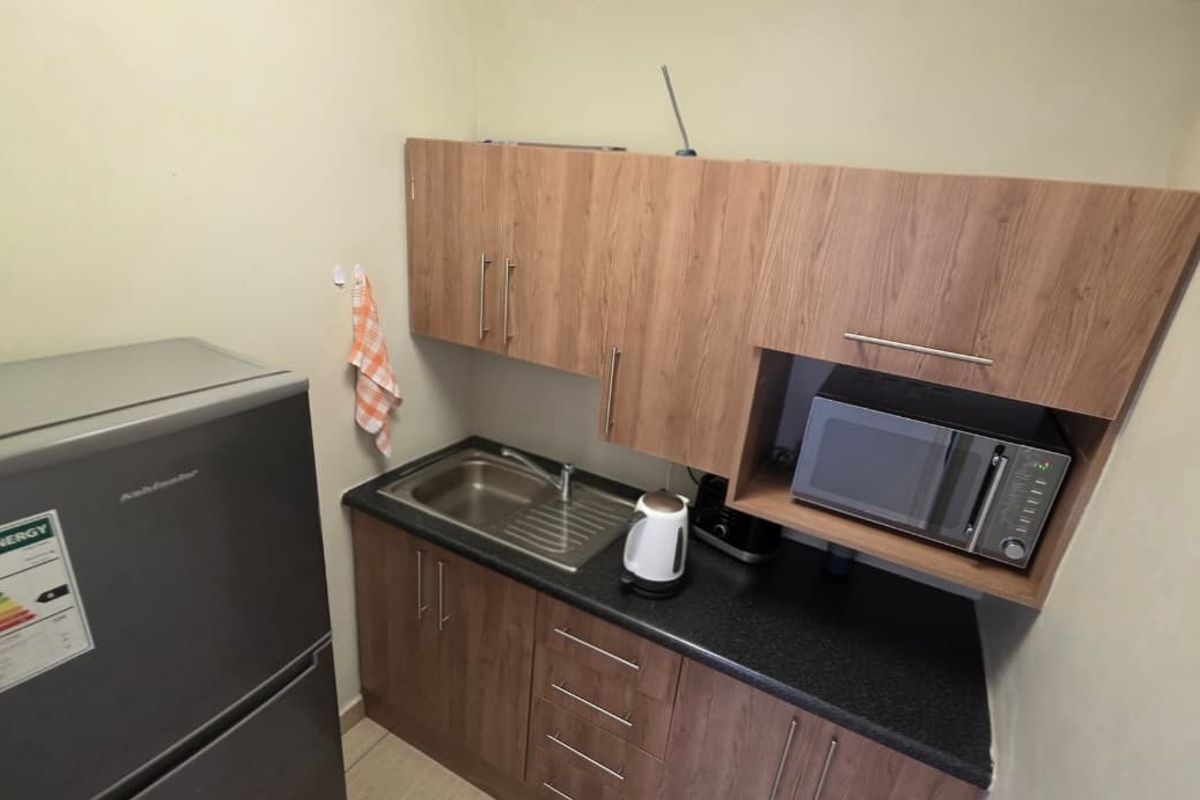 A compact office kitchenette featuring wood-finish cabinetry, a dark laminate countertop, a stainless steel sink, and a built-in microwave.