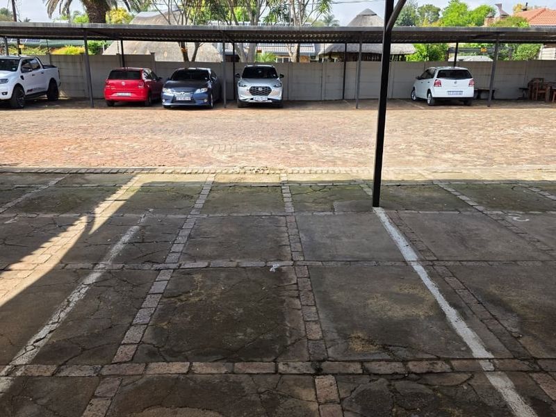 An outdoor paved parking area featuring multiple covered bays and a perimeter wall, providing ample space for office vehicle storage.