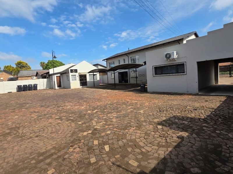 Spacious paved rear courtyard area featuring a carport, exterior wall-mounted air conditioning unit, and secure boundary walls for this office property.