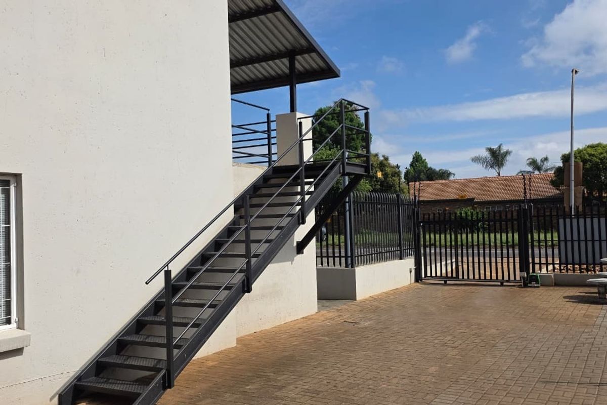 Exterior view of the office property featuring a modern metal staircase, paved driveway, and secure perimeter fencing with a sliding gate.