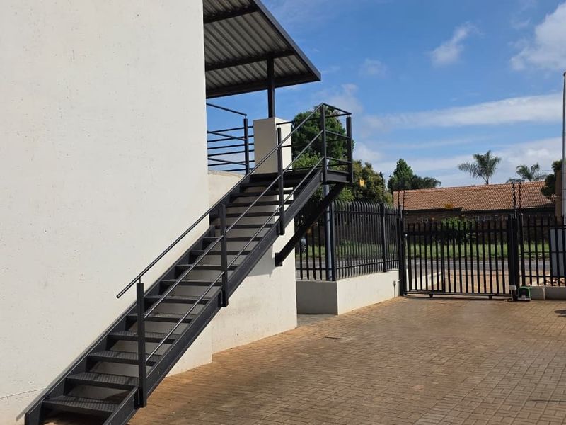 Exterior view of the office property featuring a modern metal staircase, paved driveway, and secure perimeter fencing with a sliding gate.