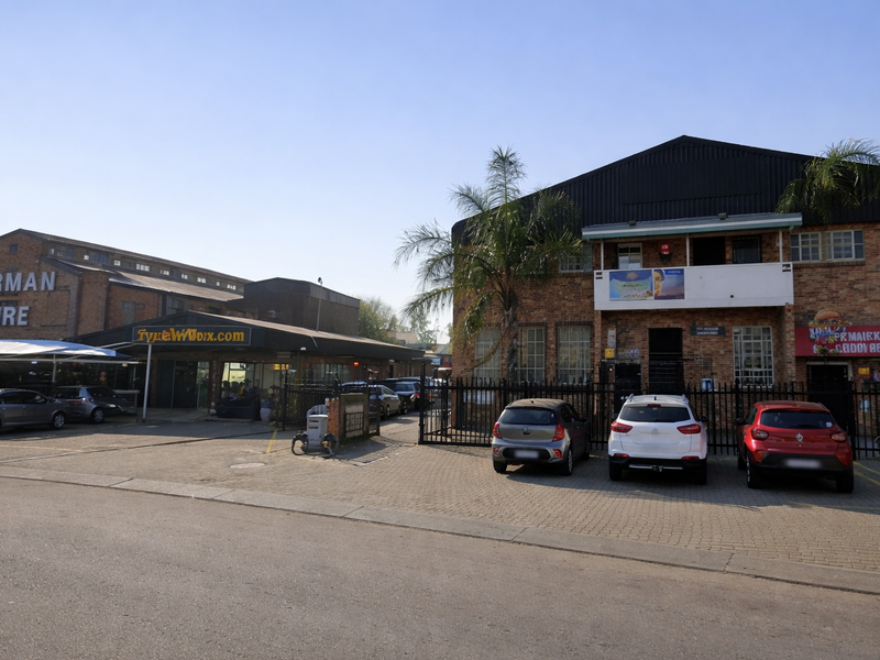 Front view of an industrial complex featuring brick facades, metal roofing, and a paved parking area with secure perimeter fencing.