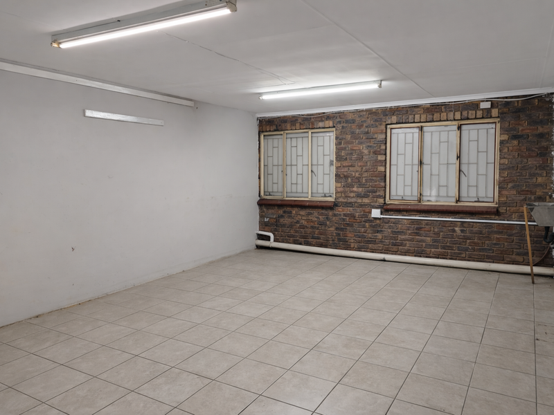 A clean, empty utility space featuring tiled flooring, exposed brick walls, fluorescent lighting, and a functional utility sink.