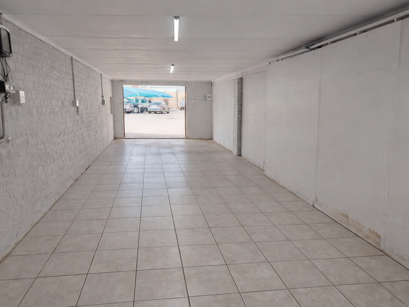 A spacious, empty industrial garage featuring tiled flooring, white painted brick walls, and overhead fluorescent lighting, suitable for storage or workshop use.