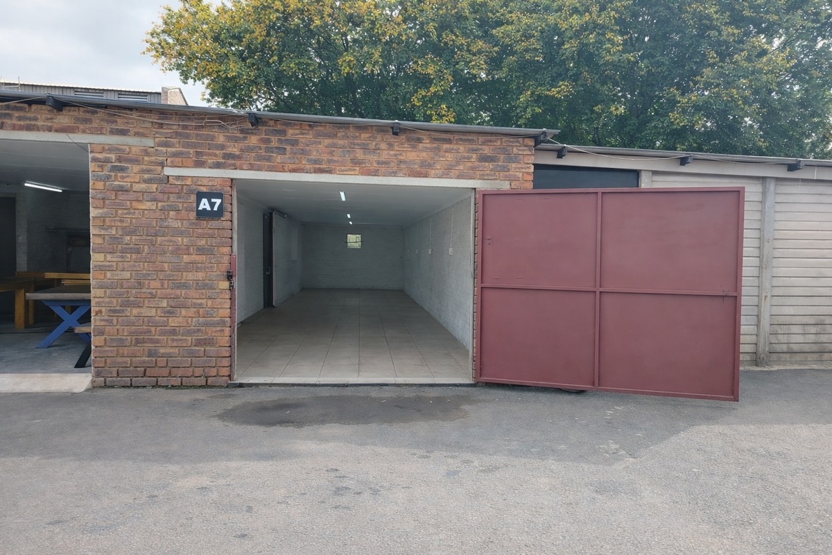 Industrial garage unit featuring brick exterior, large metal swing door, tiled interior flooring, and overhead fluorescent lighting.