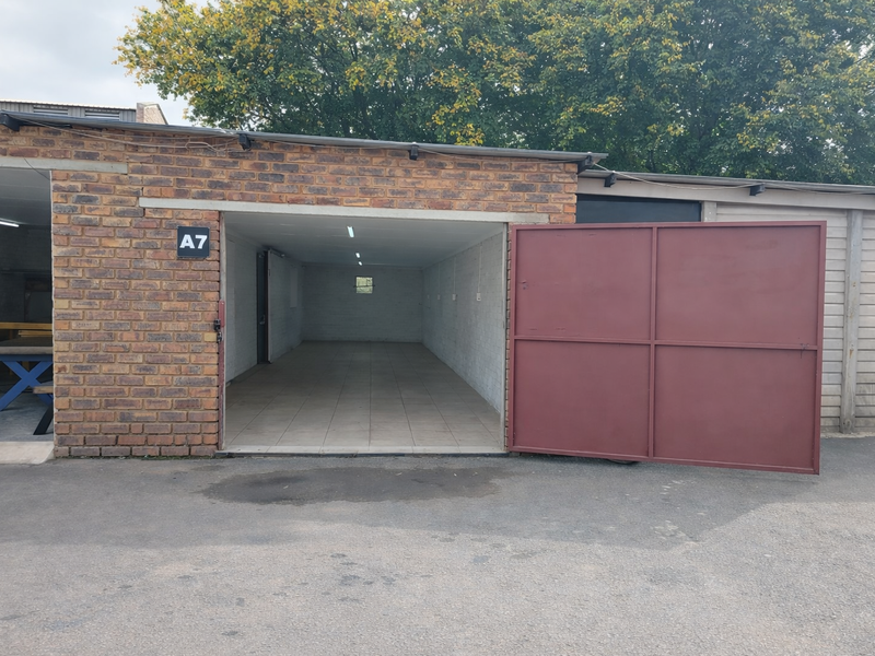 Industrial garage unit featuring brick exterior, large metal swing door, tiled interior flooring, and overhead fluorescent lighting.