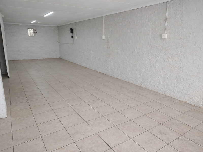 A clean, empty utility space featuring painted brick walls, ceramic tiled flooring, and functional overhead fluorescent lighting, suitable for storage or workshop use.