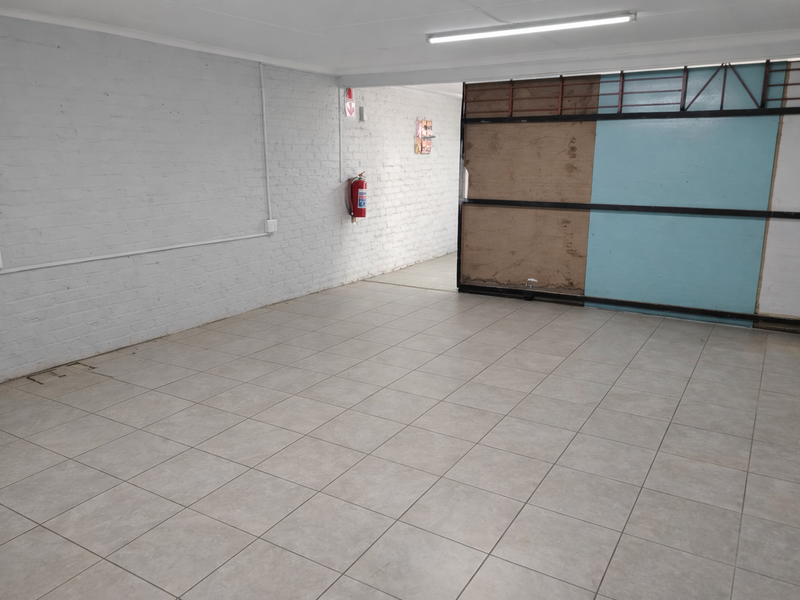 A spacious, empty industrial garage featuring tiled flooring, painted brick walls, and a large sliding metal door, suitable for storage or workshop use.
