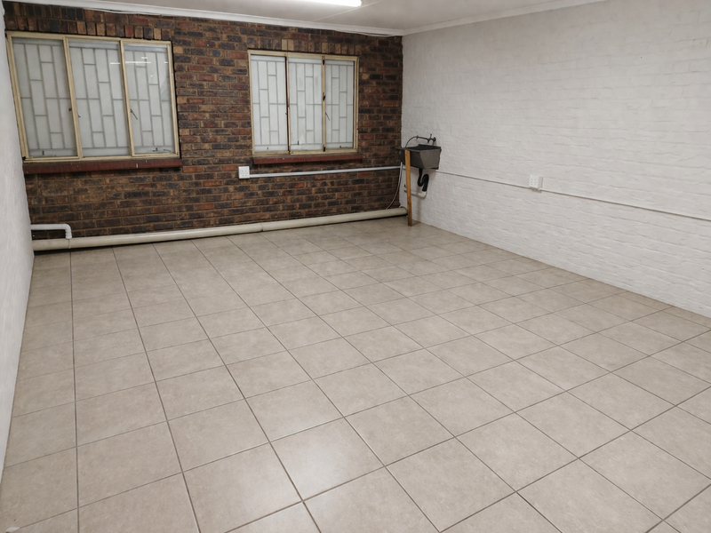A functional utility space featuring tiled flooring, exposed brickwork, security-barred windows, and a wall-mounted utility sink with exposed plumbing.