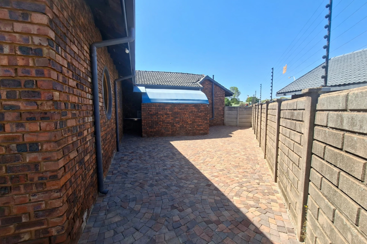 A well-maintained rear exterior area featuring brick paving, face brick walls, and secure perimeter fencing with an electric security system.