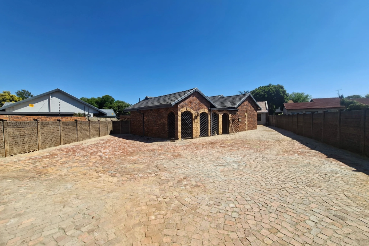 A well-maintained office building featuring a face brick exterior, tiled roof, and a spacious paved driveway enclosed by perimeter walls.