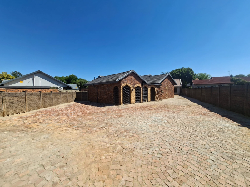A well-maintained office building featuring a face brick exterior, tiled roof, and a spacious paved driveway enclosed by perimeter walls.