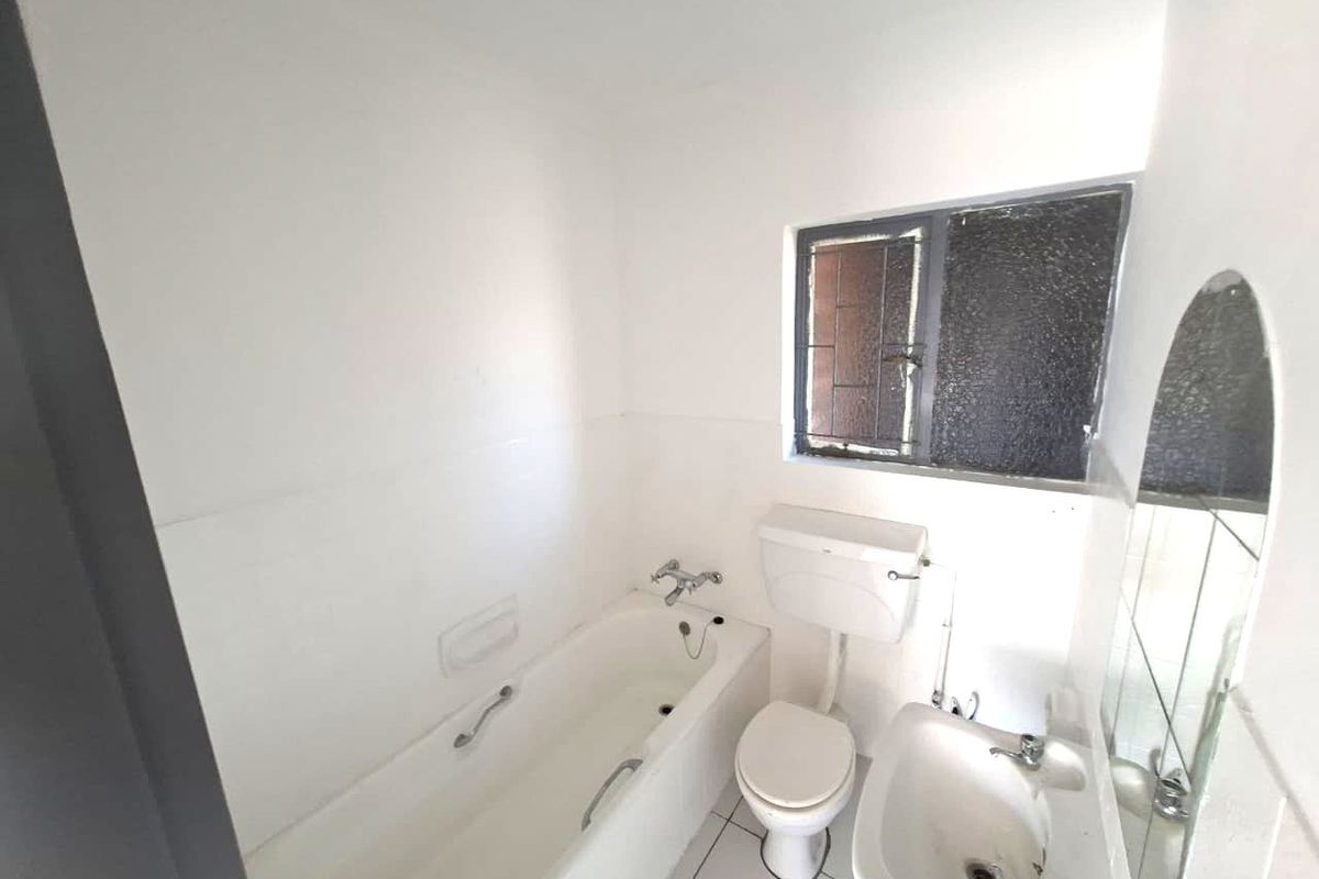 A functional bathroom featuring a standard bathtub, toilet, and pedestal basin with tiled flooring and an obscured glass window.