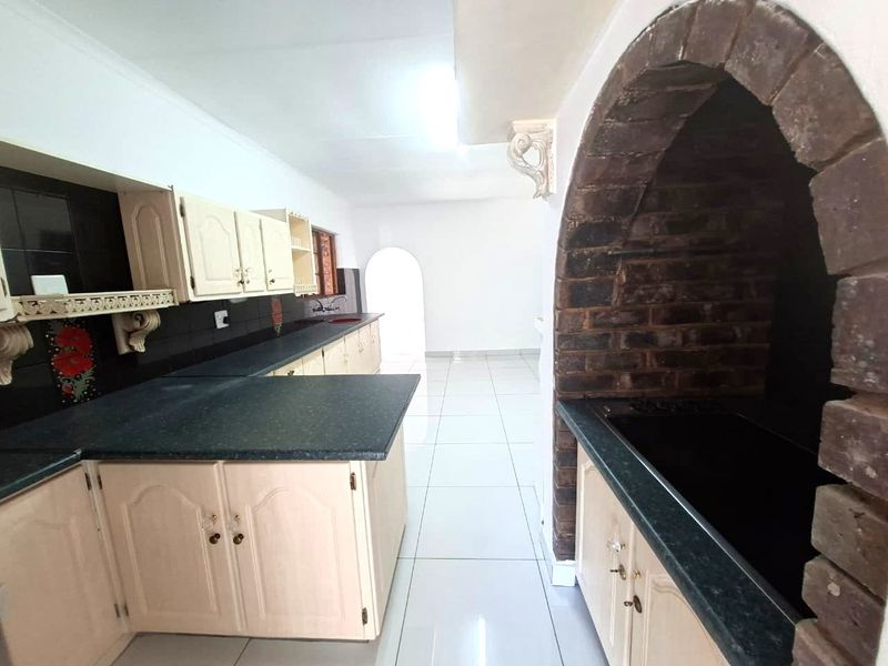 A spacious kitchen featuring built-in cabinetry, a distinctive brick archway, and tiled flooring, offering a functional layout ready for modernization.