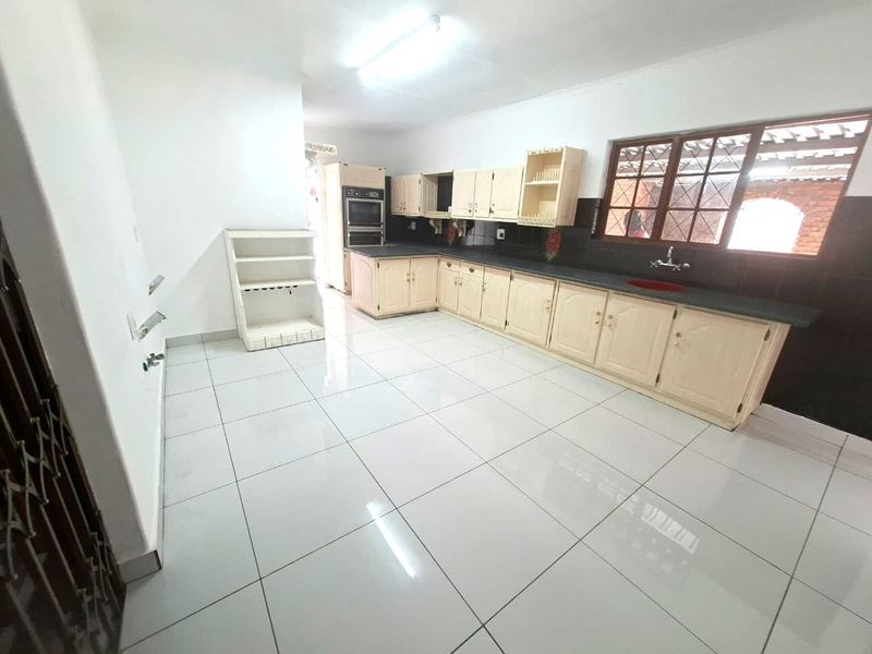 Spacious kitchen featuring light-toned built-in cabinetry, a double wall oven, tiled flooring, and a large window providing natural light.