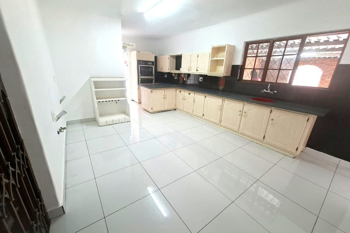 Spacious kitchen featuring light-toned built-in cabinetry, a double wall oven, tiled flooring, and a large window providing natural light.