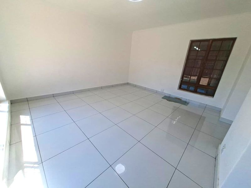 A bright, empty office space featuring clean white walls and modern tiled flooring with a timber-framed window.