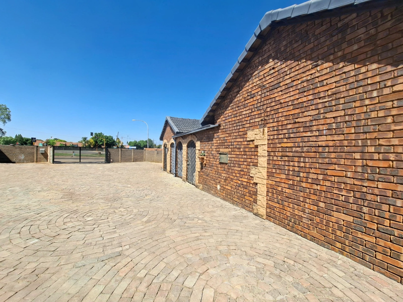 A well-maintained office exterior featuring a face brick facade, a spacious circular pattern paved driveway, and secure perimeter walling with a metal gate.