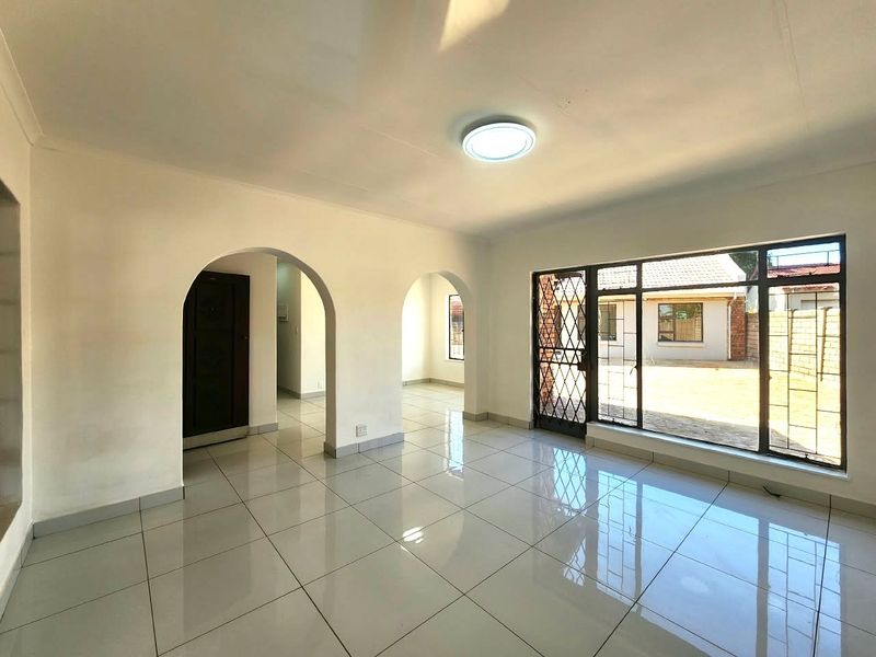 Bright and spacious living area featuring neutral tiled flooring, elegant arched architectural details, and large windows providing ample natural light.