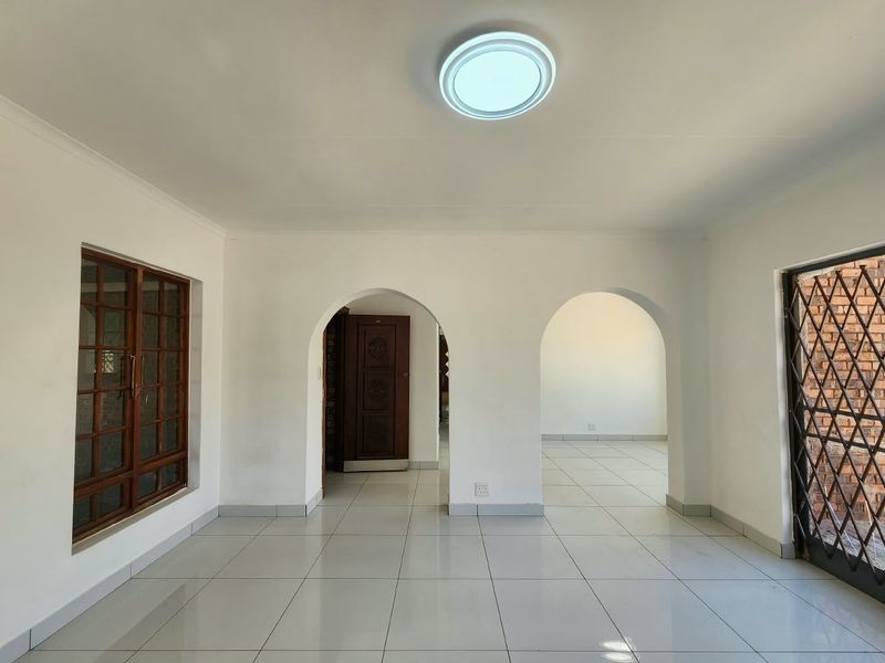 A bright, vacant office space featuring clean tiled flooring, distinctive arched doorways, and natural light through a wooden-framed window.
