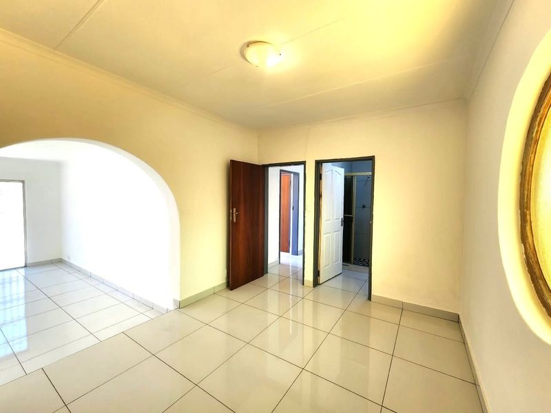 An empty office space featuring tiled flooring, a decorative archway, and neutral walls, providing a clean and versatile work environment.