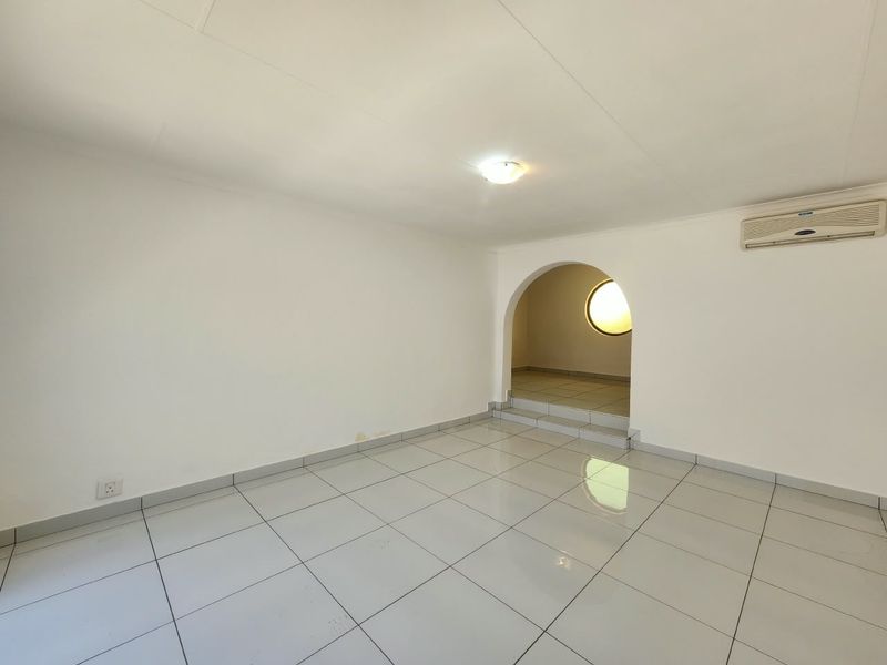 An empty office space featuring white tiled flooring, a distinctive arched entryway leading to a secondary area with a circular window, and air conditioning.