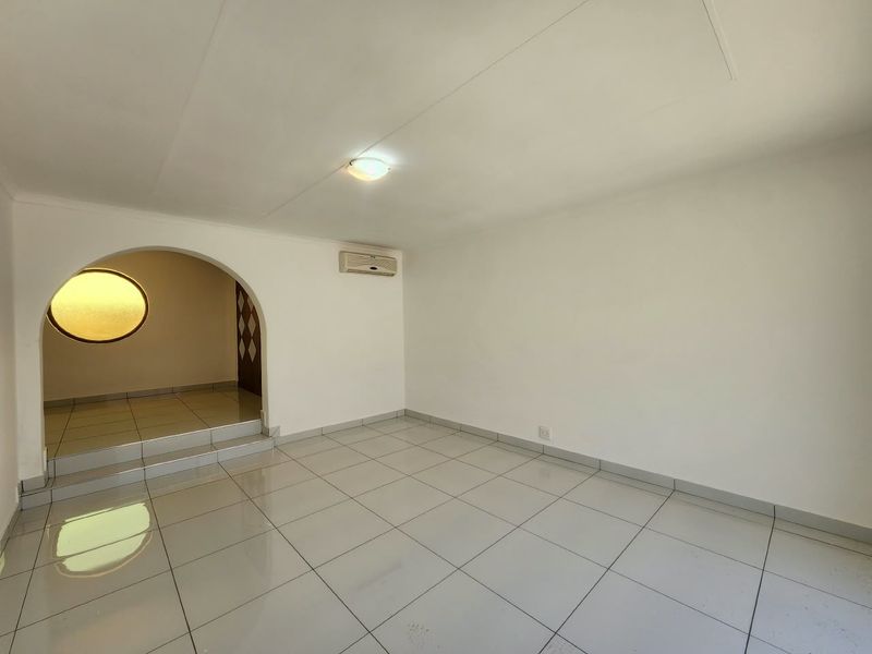 A bright, empty office space featuring tiled flooring, a distinctive arched entryway, and a wall-mounted air conditioning unit.