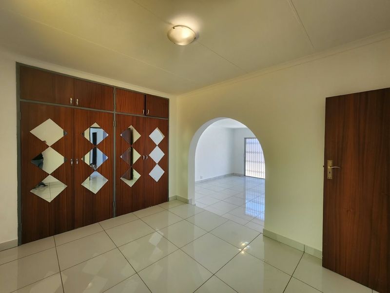 A bright, empty office space featuring tiled flooring, a decorative archway, and extensive built-in wooden cabinetry with mirrored accents.