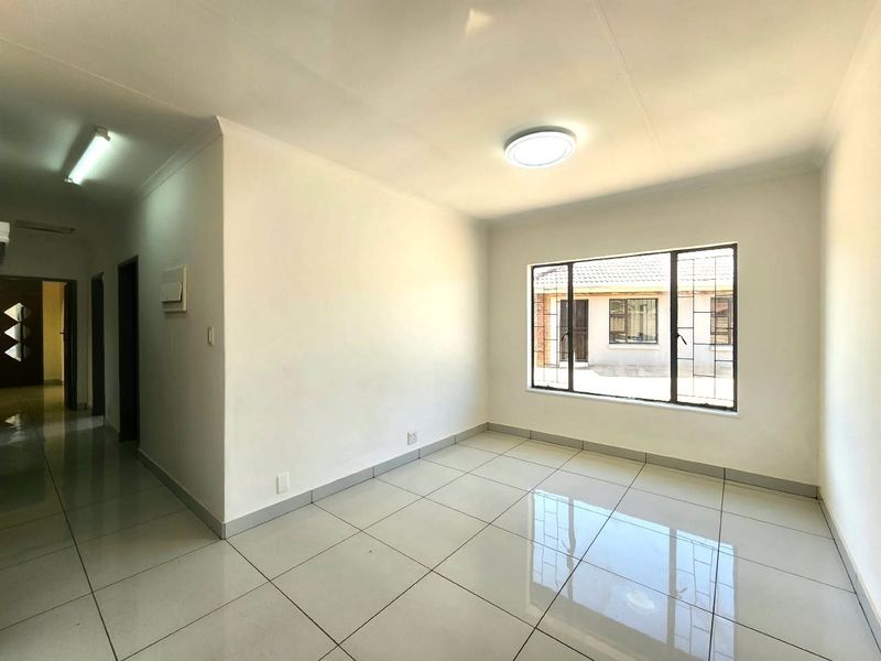A bright, empty office space featuring clean tiled flooring, neutral walls, and large windows with security bars, offering a versatile workspace.