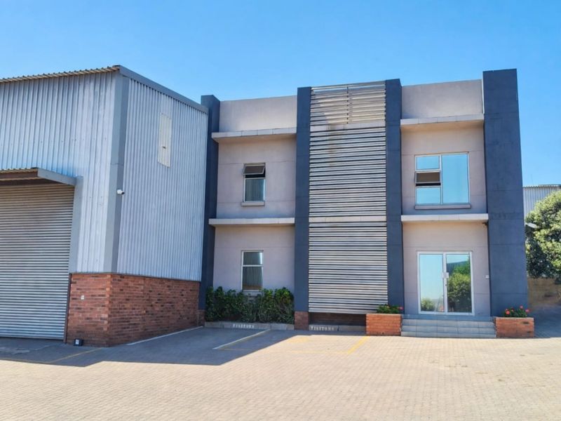 Front elevation of a modern office building featuring a combination of corrugated metal cladding, brickwork, and a paved visitor parking area.