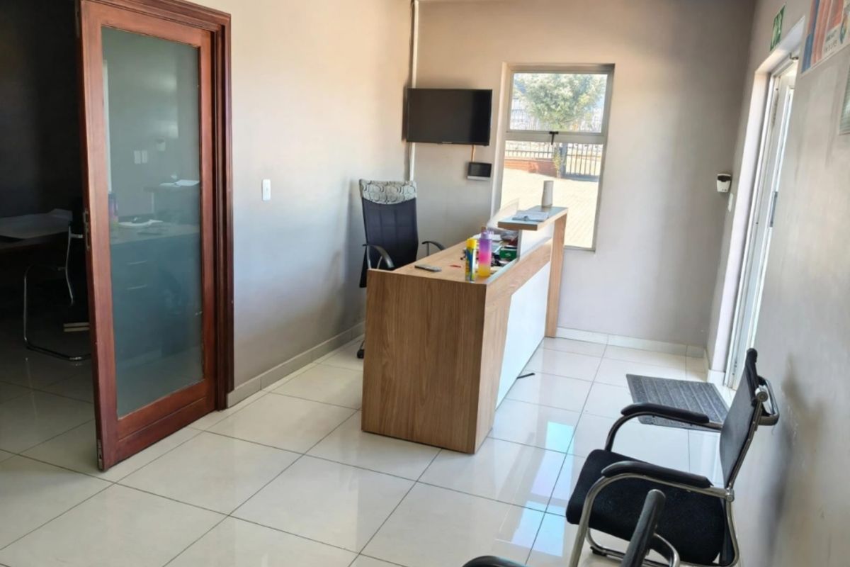 A functional office reception area featuring tiled flooring, a built-in reception desk, and a frosted glass sliding door leading to an adjacent workspace.
