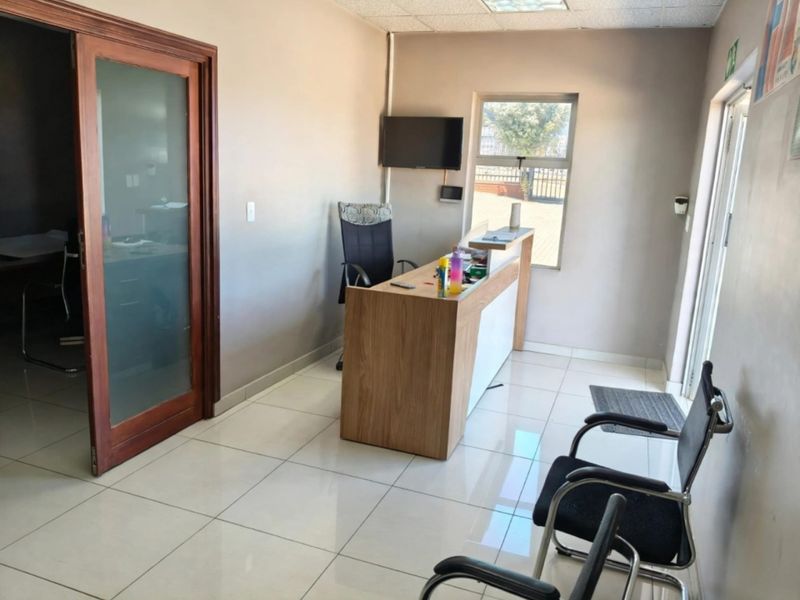 A functional office reception area featuring tiled flooring, a built-in reception desk, and a frosted glass sliding door leading to an adjacent workspace.