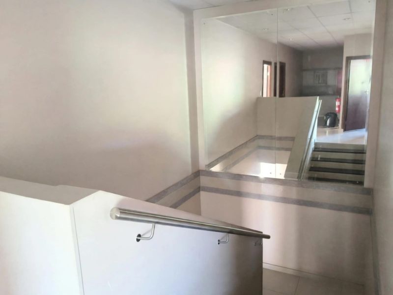 A clean, modern office hallway featuring a staircase with a stainless steel handrail and glass balustrade, leading to an upper level.
