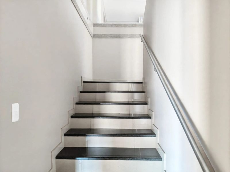 A clean, well-maintained interior staircase featuring tiled steps with contrasting dark treads and a sturdy metal handrail.