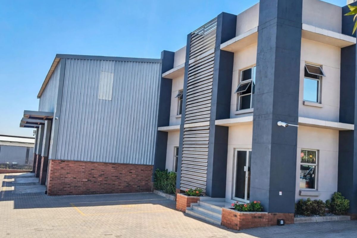 Modern commercial office building featuring a combination of brickwork, metal cladding, and large aluminum windows with a paved entrance area.